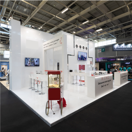 Stand d'exposition moderne avec des comptoirs, des chaises blanches et un popcorn d'appoint.
