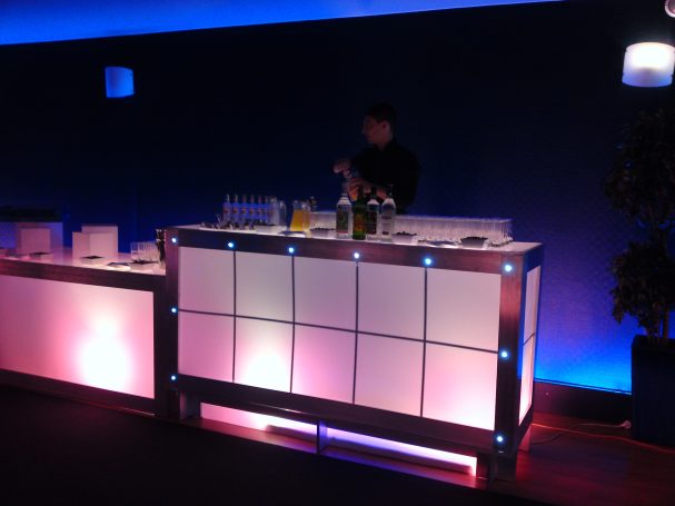 Bar lumineux avec un barman préparant des boissons. Ambiance moderne et colorée.