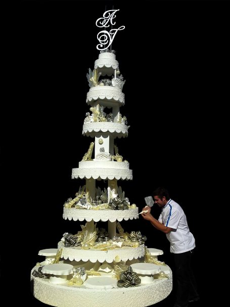Gâteau de mariage en étages, décoré avec des pompons et des figurines sur fond noir.