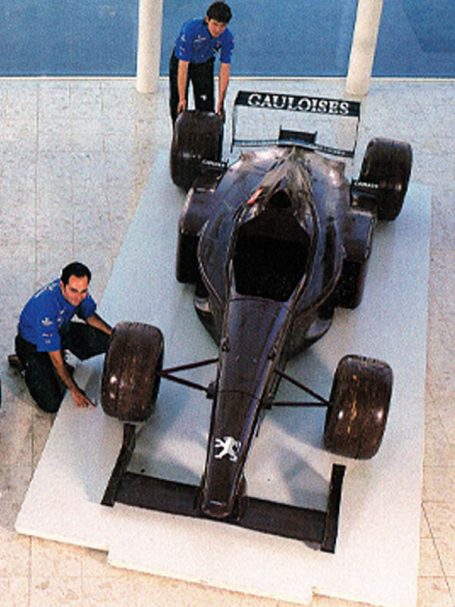 Deux techniciens ajustent une voiture de course noire sur un socle.