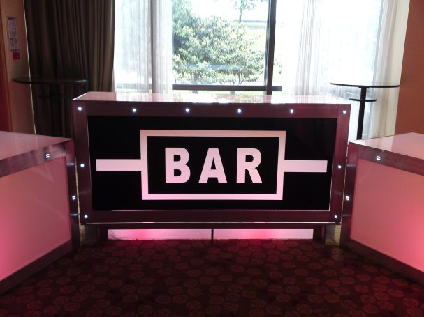  Comptoir de bar lumineux avec le mot "BAR" en lettres blanches sur fond noir.